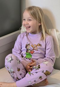 Lila långärmad pyjamas med en tecknad kattdesign på tröjan och färgglada mönster av djur och växter på byxorna.