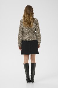 Langärmliges Oberteil im Leopardenmuster kombiniert mit einem schwarzen Jeans-Minirock und hohen schwarzen Stiefeln. Glatte Textur mit ausgeprägten Mustern.