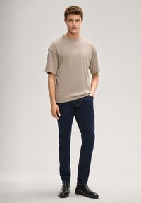 Beżowy t-shirt z krótkim rękawem w połączeniu z ciemnoniebieskimi jeansami o dopasowanym kroju oraz czarnymi botkami za kostkę. Gładka tkanina, luźny krój i prosty design.