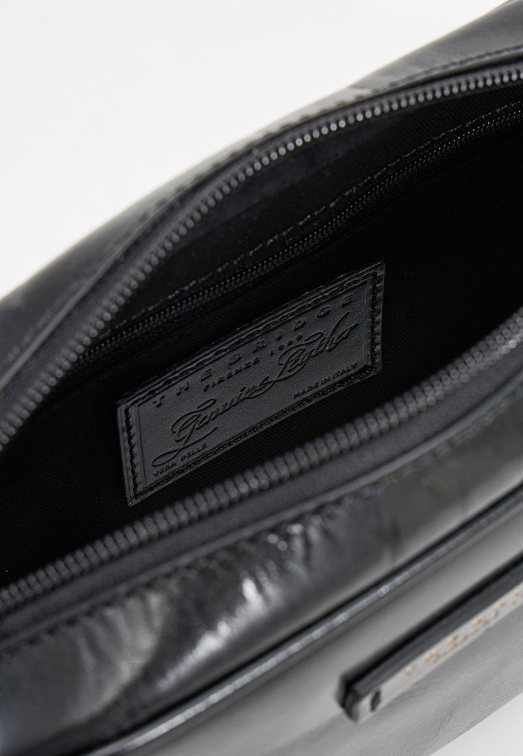 Interno di una borsa in pelle nera con chiusura a zip, caratterizzato da una texture liscia e un'etichetta del marchio visibile sull'imbottitura.
