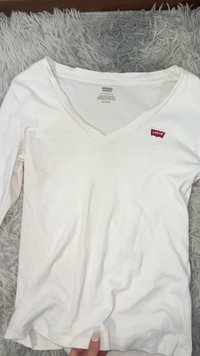 Maglietta a maniche lunghe bianca con scollo a V in cotone con logo Levi's rosso sul petto a sinistra. Texture liscia e vestibilità casual.