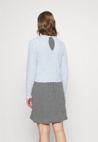 Suéter de punto acanalado en azul claro con detalle de apertura en la espalda, combinado con una falda de patrón de ajedrez en blanco y negro.