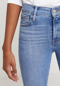 Jeans in denim blu chiaro con vita alta, dotati di cinque tasche, sbiaditure leggere e cuciture in contrasto. Il tessuto appare morbido e liscio.