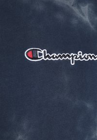 Tmavě námořnické tričko s jemným batikovacím efektem. Na přední straně je vyšitý logo Champion v bílé, červené a modré barvě.