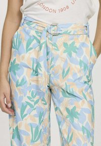 Pantalon bleu clair avec un motif floral dans des tons de vert et de beige. Dispose d'un détail de nouage à l'avant et d'une boucle en argent. Fabriqué en tissu doux.