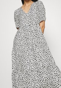 Czarna i biała sukienka z dekoltem w kształcie litery V, krótkimi puffowanymi rękawkami oraz warstwowym fasonem z wzorem serduszek na całej powierzchni. Miękka, lekka tkanina.