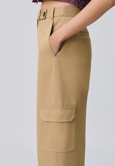 Pantaloni beige realizzati in tessuto liscio, con tasca laterale, chiusura frontale con bottone e vestibilità sartoriale, visibili in vista laterale.