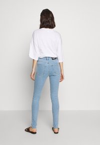 Ljust blå skinny jeans i denim, med hög midja, bakfickor och en svart märkeslapp på midjebandet, kombinerade med en vit skjorta.