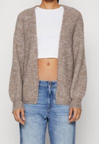 Brązowy sweter dzianinowy z otwartym przodem, rękawami o prążkowanej strukturze i miękką teksturą, noszony na białej topie z krótkim rękawem i niebieskich dżinsach.