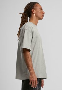 Šedé oversized tričko vyrobené z bavlny, s krátkymi rukávmi, okrúhlym výstrihom a voľným strihom. Hladká textúra s minimálnym detailovaním.