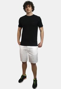 T-shirt nera in cotone, pantaloni corti bianchi con cordino e scarpe da ginnastica nere con accenti neon. Posizione in piedi, sfondo neutro.
