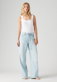 Calças de ganga largas azul claro com cintura elástica e bolsos frontais, combinadas com um top justo branco. Textura suave, ajuste casual.