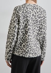 Sweat-shirt gris avec motif léopard noir, manches longues, poignets côtelés et encolure arrondie, fabriqué dans un tissu doux et texturé.