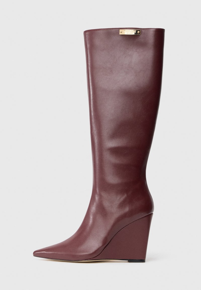 Tall burgundy leather wedge boot with pointed toe and gold brand plaque near the top edge.