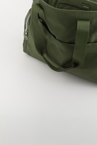 Dark green fabric bag with dual handles, a side silver zipper, and a small front pocket on a white surface.