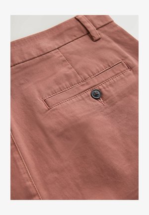 Rosenfarvede bukser med en glat tekstur, en baglomme og en sort knapdetalje. Stoffet virker let og lidt skinnende.