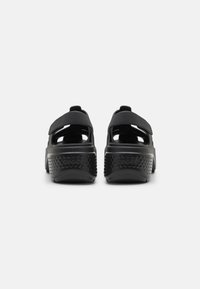 Sandales noires au design ouvert, en matériau doux, avec des sangles ajustables et des semelles texturées présentant de petits motifs ronds pour une bonne adhérence.