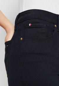 Jeans in denim nero con un design aderente. Presentano accessori in oro, una piccola tasca con dettagli rosso, bianco e blu, e un'apertura per la tasca laterale.