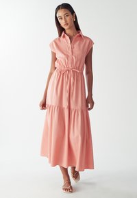 Różowa sukienka zapinana na guziki, z krótkimi rękawami, podkreśloną talią i warstwowym dołem. Wykonana z lekkiego materiału o gładkiej teksturze.