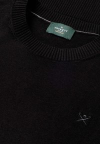 Black knit sweater with ribbed crew neckline, small embroidered crossed cane and hat logo, and green Hackett London Heritage label inside collar.