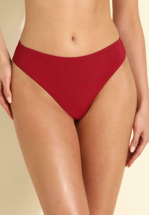 Kobieta w jednolitych czerwonych majtkach bikini, pokazana od połowy tułowia do połowy uda na neutralnym tle.