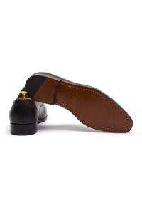 Scarpe eleganti in pelle marrone, che mostrano un design elegante, con una finitura liscia e una suola di un marrone chiaro a contrasto. Presenti dettagli in oro.