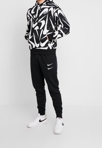 Svartvitt abstrakt mönstrad hoodie med framficka, parat med svarta joggers med vita Nike-loggor och vita sneakers.