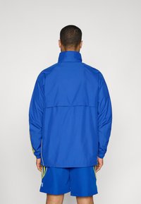 Blauwe windjack met een hoge kraag, lange mouwen en groene zijkanten. Gladde textuur, ontworpen voor een sportieve pasvorm.