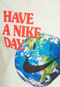 Valkoinen t-paita, jossa on sininen ja vihreä maapallon graafinen kuva mustalla hymyllä ja Nike-logolla alla punaisella tekstillä, jossa lukee "HAVE A NIKE DAY."