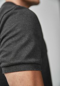 Kortærmet, mørkegrå t-shirt, lavet af blødt stof, med en tætsiddende pasform og subtil tekstur på skulder- og armområderne.