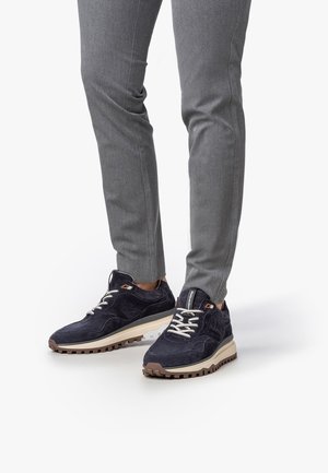 Zapatillas de ante azul marino para hombre con suela de goma beige y cordones blancos. Con detalles en relieve en la parte superior y un logo como acento.