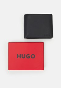 Portofel din piele neagră cu logo-ul „HUGO” embossat, expus pe o cutie roșie cu același logo în litere negre.