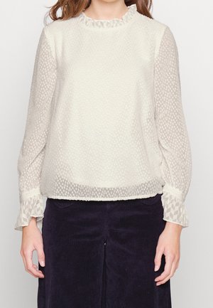 Blusa crema chiaro con tessuto texturizzato, scollatura arricciata e maniche lunghe trasparenti con un motivo geometrico ai polsini.