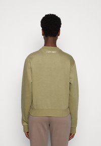 Sudadera de color verde oliva con cuello redondo, dobladillo y puños acanalados. Presenta un pequeño bordado "EST.1981" en la parte superior de la espalda. Textura suave.