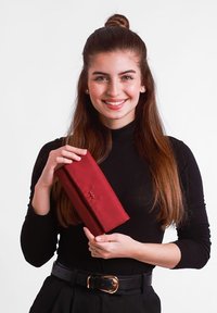 Burgundy wallet made of smooth leather, featuring a subtle embossed logo. Held by a person in a black turtleneck, with long brown hair.