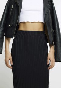 Czarna prążkowana spódnica midi z wysokim stanem, zestawiona z krótkim białym topem i czarną skórzaną kurtką z suwakiem i kieszeniami.
