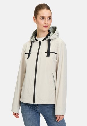 Leichte, beige Jacke mit Kapuze, schwarzen Reißverschlüssen und kontrastierenden Akzenten. Sie hat eine glatte Textur und bietet eine lockere Passform.