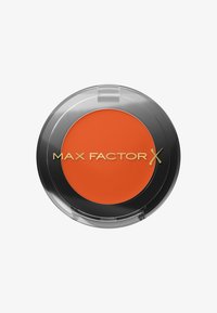 Max Factor X oranssi kerma-punastus hienossa, pyöreässä läpinäkyvässä pakkauksessa, jossa on sileä pinta ja kohokuvioitu logo. Sisältää elävän, mattapinnan.