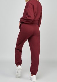 Conjunto de sudadera burdeos y joggers a juego en tejido suave. La sudadera tiene un diseño recortado; los joggers cuentan con puños elásticos y bolsillos laterales.
