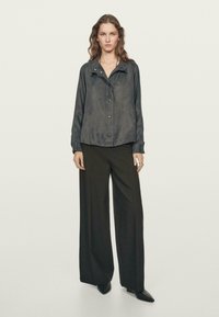 Black silk shirt with a collar and hidden buttons, paired with wide-legged black trousers and pointed black shoes, on a light background.