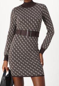 Robe en maille marron avec un motif géométrique crème, col montant, manches longues, et une large ceinture en tissu avec une boucle brillante.