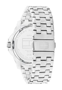 Montre-bracelet en acier inoxydable argenté avec un design de bracelet à maillons, dos transparent avec logo en relief, et fermeture carrée. Résistante à l'eau.