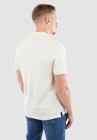 Strukturierter, weißbeiger Polo-Shirt mit Kragen, kurzen Ärmeln und seitlichen Schlitzen; kombiniert mit blauen Jeans; Rückansicht.