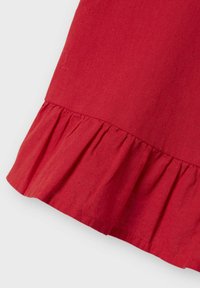 Tessuto di cotone rosso con un dettaglio a volute strutturato all'orlo, che presenta una finitura liscia e cuciture accurate.