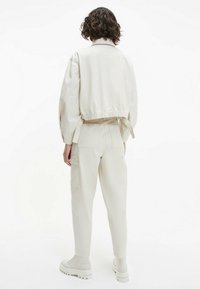 Béžová zkrácená bunda s elastickým pasem, spojená s ladícími zúženými kalhotami s cargo kapsami a bílými botami na chunky podešvi.