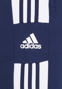 Marineblå sweatshirt med vitt Adidas-logotyp och tre vita ränder på övre vänstra sidan. Mjuk tyg med en texturerad yta.