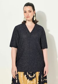 Granatowa bluzka z dekoltem w serek i krótkimi rękawami, wykonana z teksturowanej tkaniny. Połączona z żółtą plisowaną spódnicą w abstrakcyjne wzory w ciemniejszych odcieniach.