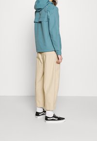 Niebieska kurtka z kapturem, beżowe luźne spodnie i czarne sneakersy. Kurtka ma gładką teksturę, a spodnie charakteryzują się luźnym krojem.