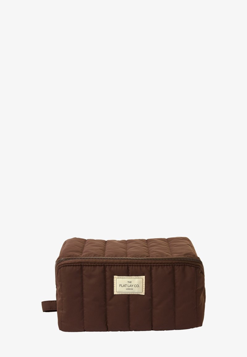 Braune, gesteppte Kosmetiktasche mit rechteckiger Form, Reißverschluss und einem Stoffetikett auf der Vorderseite. Glatte Textur und gepolstertes Design.