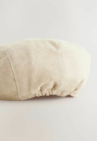 Rundes Kissen aus hellbeigem Stoff mit strukturierter Oberfläche und gerafftem Nahtdetail am Rand.